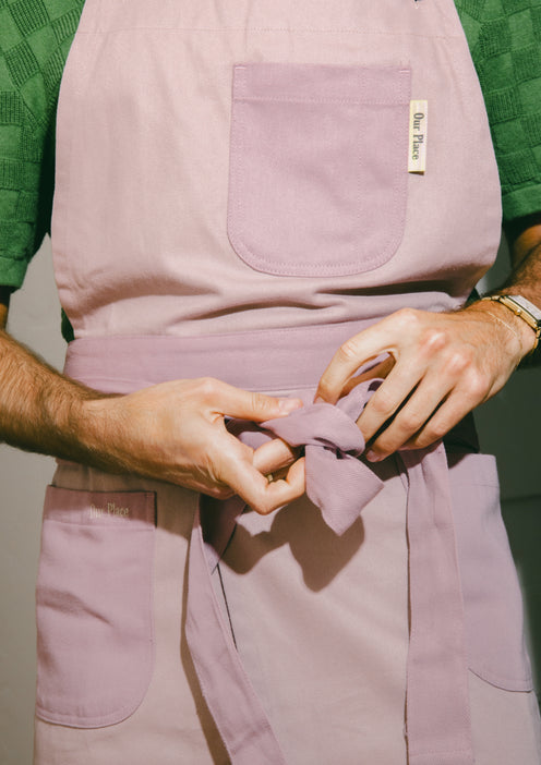 A chef wearing a purple Home Cook Apron ties the apron around the body
