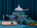 Assorted cookware and kitchen utensils arranged with wrapped gifts and decorative bows on a blue fabric backdrop.