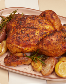 A whole roasted chicken seasoned with herbs, served on a platter with roasted potatoes and garnished with rosemary.