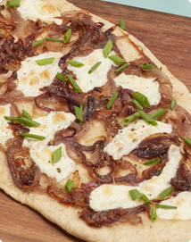 Flatbread topped with caramelized onions, melted cheese, and chopped green onions on a wooden board.