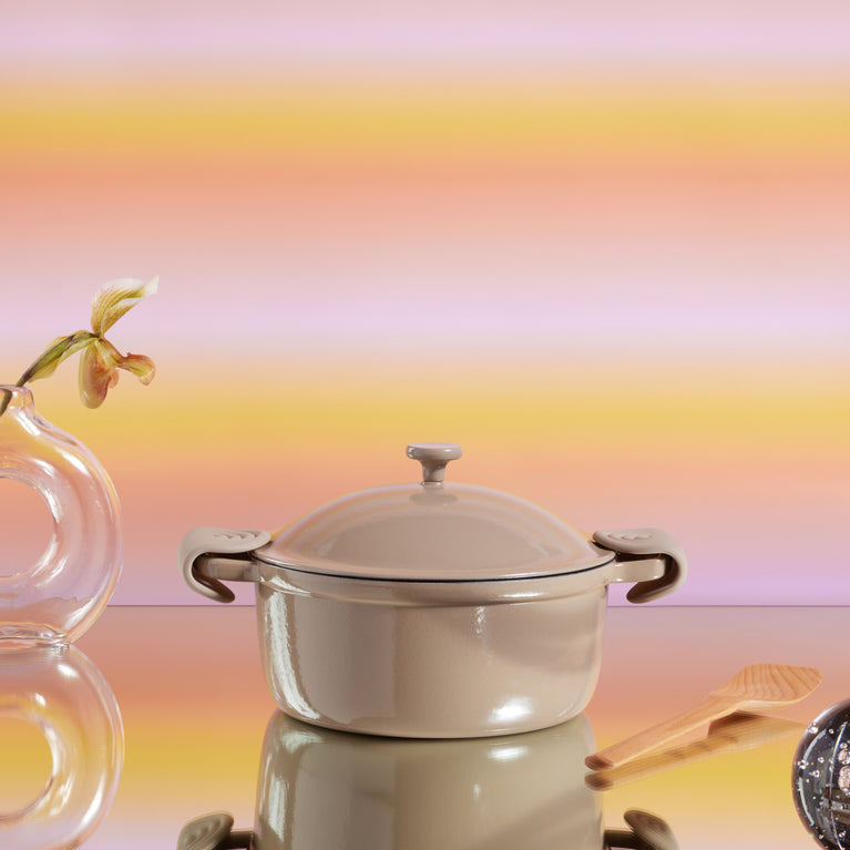 Beige Cast Iron Perfect Pot with scraper and hot grips on pink background