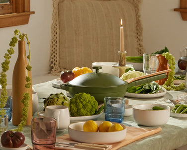 A dining table decorated with white dinnerware, colorful drinking glasses, food, and candles