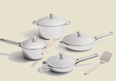 Set of white cookware with lids and utensils on a beige background