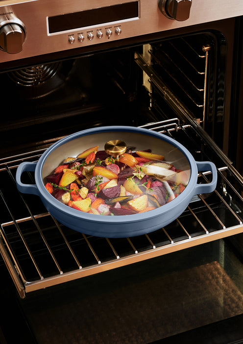 A round pan filled with chopped vegetables and herbs is placed on a rack inside an open oven.