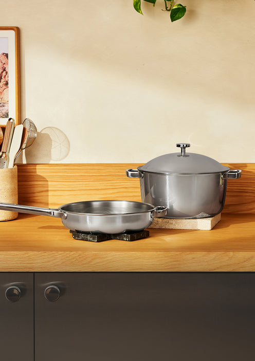 A stainless steel skillet and a lidded stockpot on a wooden kitchen counter.