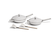 Two stainless steel frying pans with lids and two white spatulas are displayed on a white surface.