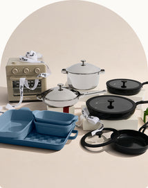 Collection of cookware including pots, pans, and a small oven on a beige background.