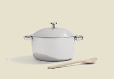 White enameled cast iron cookware with a wooden spoon on a beige background
