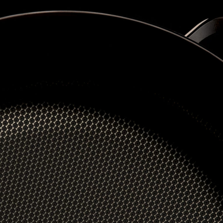 Close-up of the textured, nonstick surface of a dark frying pan with part of the curved rim and handle visible against a black background.