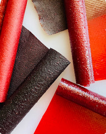 Several fruit leather rolls in shades of red and dark purple arranged on a white surface.