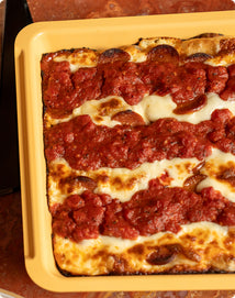 Rectangular pepperoni pizza with stripes of melted cheese and tomato sauce in a yellow baking dish.