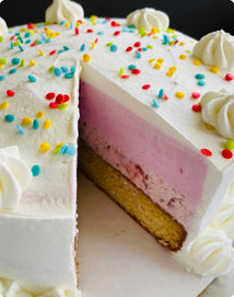 A layered ice cream cake with a sponge base, strawberry ice cream, and white frosting topped with sprinkles and piped cream rosettes, with one slice removed.