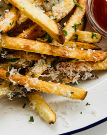 French fries topped with grated cheese and herbs, served with a side of dipping sauce.