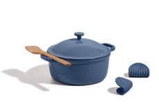 A blue Dutch oven with a lid, a wooden spatula resting on top, and two blue silicone pot holders on a white background.