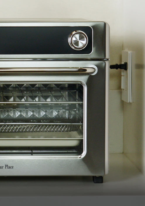 A stainless steel countertop oven plugged into a wall outlet.