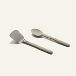 A Titanium Pro Utensil Set featuring a metal spatula and a solid-colored spoon side by side.