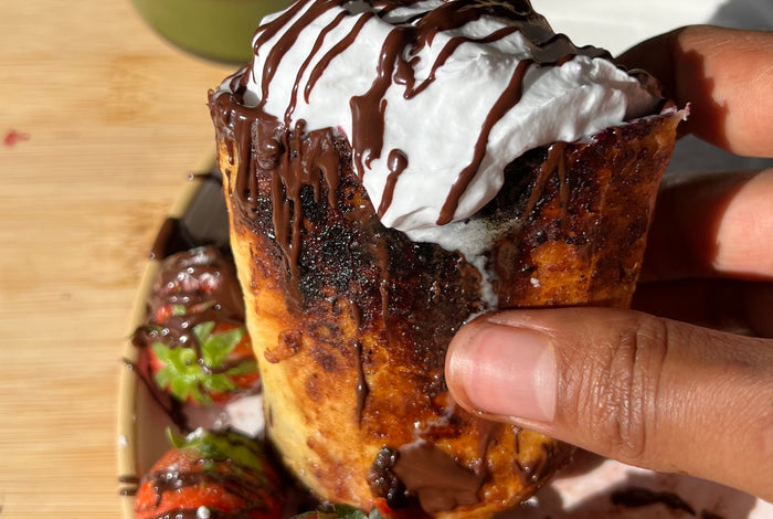 A photo of a hand holding a french toast burrito with cream on top