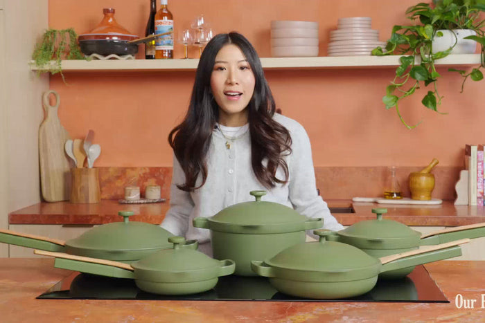 Woman standing in behind a counter with green pots and pans in front of her