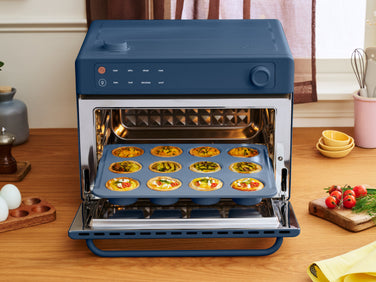 A blue countertop oven with its door open, containing a tray of twelve baked mini quiches.