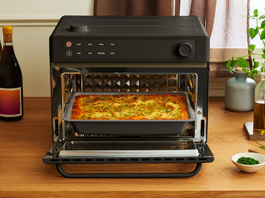 A black countertop oven with its door open, containing a rectangular baking dish filled with a baked potato dish.