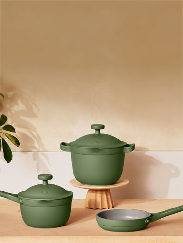 Set of green cookware including a pot, frying pan, and saucepan on a wooden surface with a kitchen background.