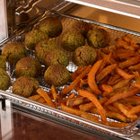 A wire basket inside an air fryer containing falafel balls and sweet potato fries.