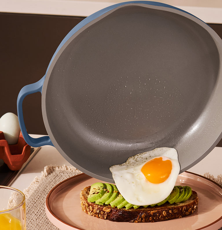 blue frying pan with blue handle on a kitchen counter with toast and avocado spread.