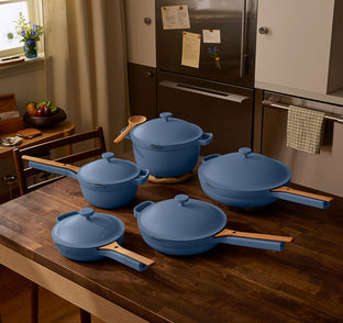 Set of blue cookware on a wooden kitchen counter with a refrigerator in the background.