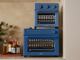 Two blue Our Place countertop ovens stacked on a kitchen counter next to bottles of oil and sauce.