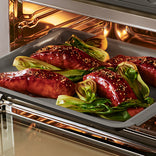 Glazed salmon fillets with bok choy on a baking tray inside an oven.