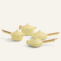 The Cookware Set includes four yellow pans with wooden handles and matching lids, inspired by the Always Pan, displayed against a plain white background.