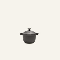 The Petite Perfect Pot is a small, matte black nonstick pot with dual handles and a matching lid, ideal for single servings, shown against a simple light background.
