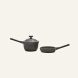 The Tiny Cookware Duo, featuring a black saucepan with lid and a black frying pan, are displayed side by side on a plain light background.