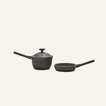 The Tiny Cookware Duo, featuring a black saucepan with lid and a black frying pan, are displayed side by side on a plain light background.