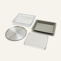 The Wonder Oven Pro Chef’s Kit features a perforated round tray, square wire rack, rectangular mesh basket, and baking pan on a plain background.