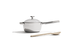 A white saucepan with a lid and a silver handle is placed next to a beige wooden spoon on a plain white background.