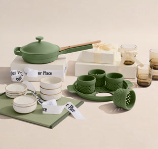 Green ceramic cookware set with matching accessories on a neutral background