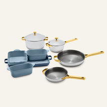 The Titanium Pro Cookware + Bakeware Set 2.0 features silver pots and pans with gold handles, alongside blue ceramic bakeware dishes.