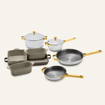 Titanium Pro Cookware + Bakeware Set 2.0 featuring two silver pots with lids, two silver skillets, and four gray rectangular ceramic bakeware pans, all with metallic gold handles.
