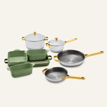 Titanium Pro Cookware + Bakeware Set 2.0 featuring silver-toned pots with lids, two frying pans, three green ceramic bakeware dishes, and a checkerboard serving tray with gold handles.