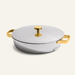 Introducing the Titanium Braiser Pro 28 cm: a round, silver casserole dish featuring a fitted lid and striking gold-colored handles and knob. Set against a plain light background, this chef-approved stainless steel braiser seamlessly blends elegance with durability.