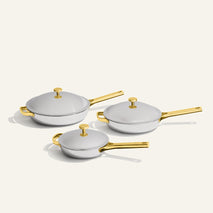 Titanium Pro Always Pan Trio 2.0: three silver-colored stainless steel pans with gold-toned handles and lids in varying sizes.