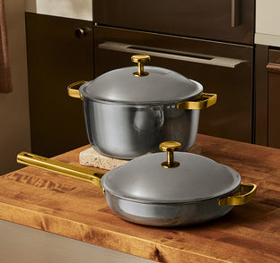 Two metallic pots with gold handles and lids sit on a wooden countertop in a modern kitchen.