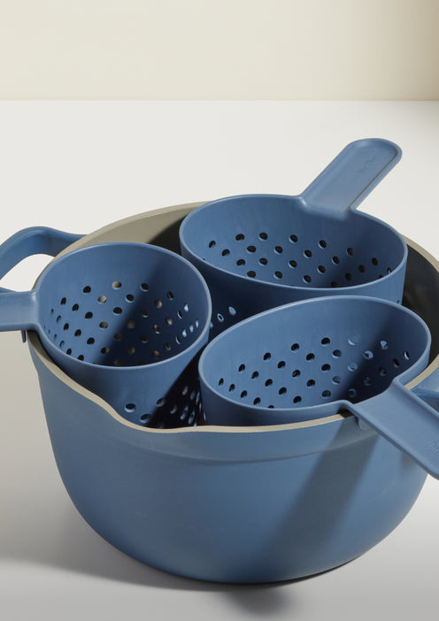 A set of three blue plastic colanders with handles stacked inside a larger blue mixing bowl on a white surface.