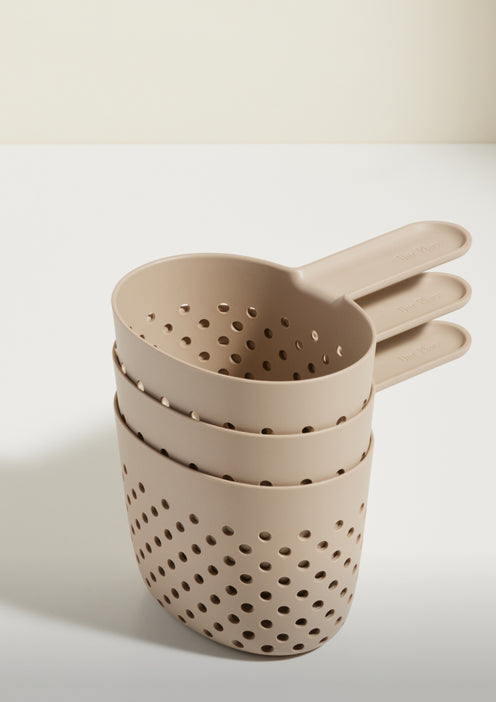 Three beige plastic colanders with handles are stacked together on a white surface against a light background.