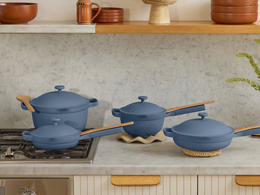 Set of blue cookware on a kitchen counter with shelves displaying terracotta pots in the background.