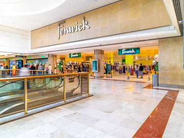 Fenwick store interior with escalator and shoppers in a shopping mall.