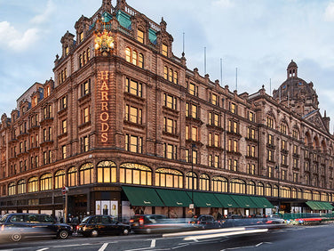 Harrods department store exterior with illuminated sign and limousines on a street.