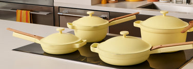 Set of yellow cookware with wooden handles on a stove in a kitchen.