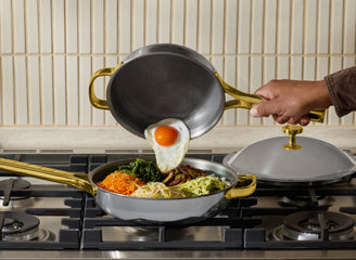 Person cooking an egg and vegetables in a frying pan on a stove.